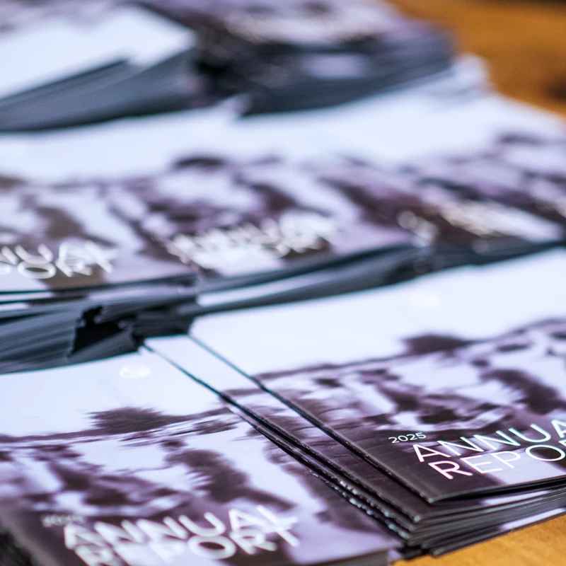 A close-up, shallow-focus photograph of stacks of printed booklets. The cover clearly reads '2025 Annual Report' in white text over a monochrome image.
